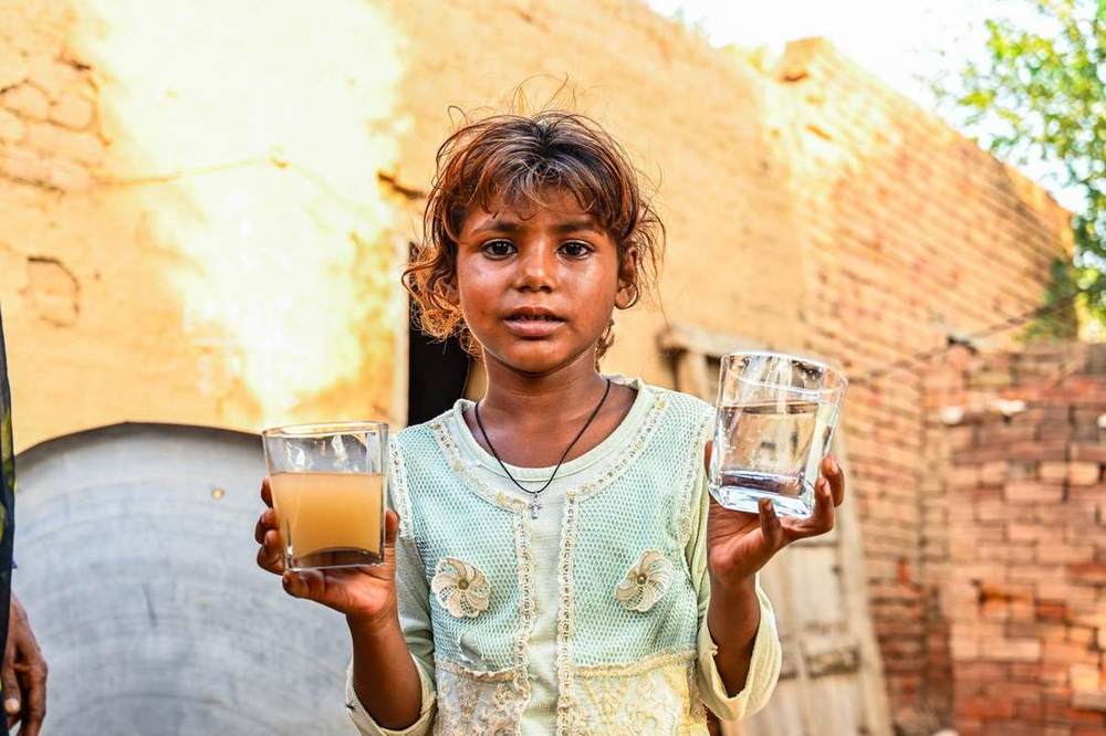 A child holding one glass of village water and one of filtered water